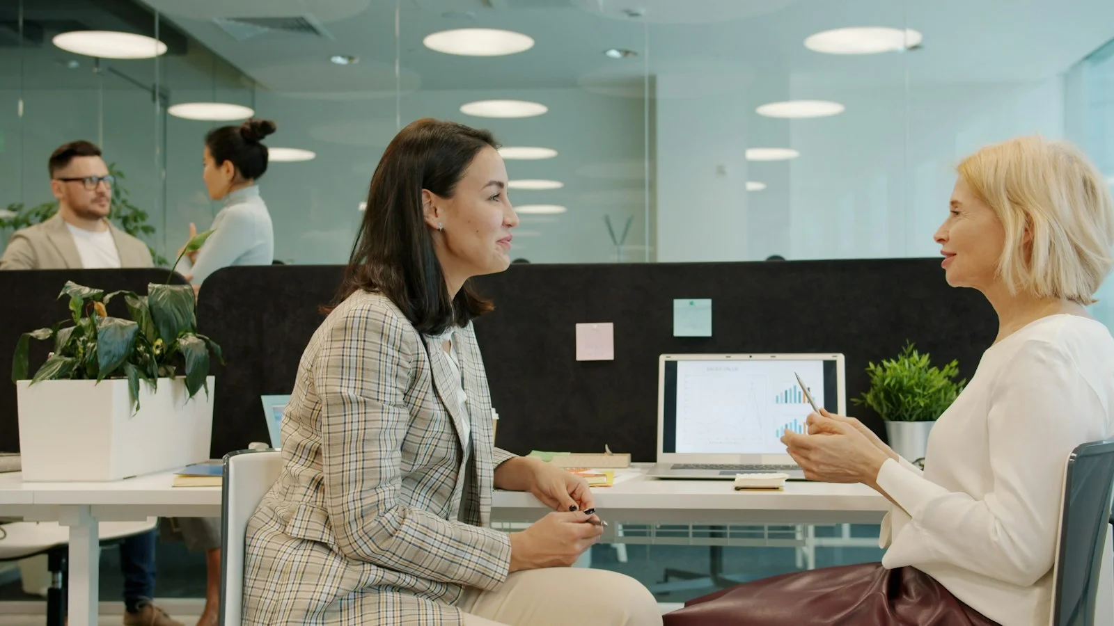 Two women talking at a desk in an open plan office